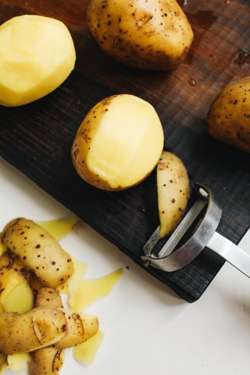 potatoes with a potato peeler on a cutting board